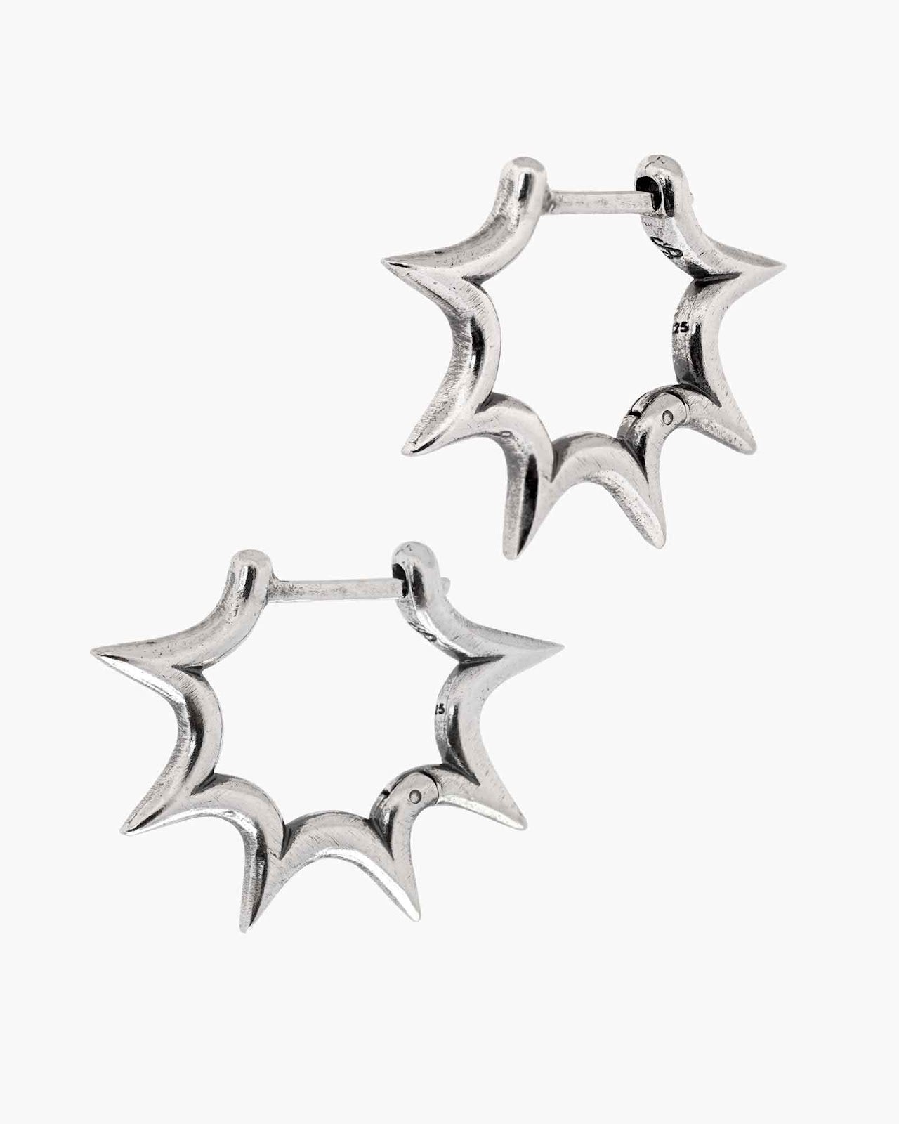 Pair of silver burst huggie earrings on a white background
