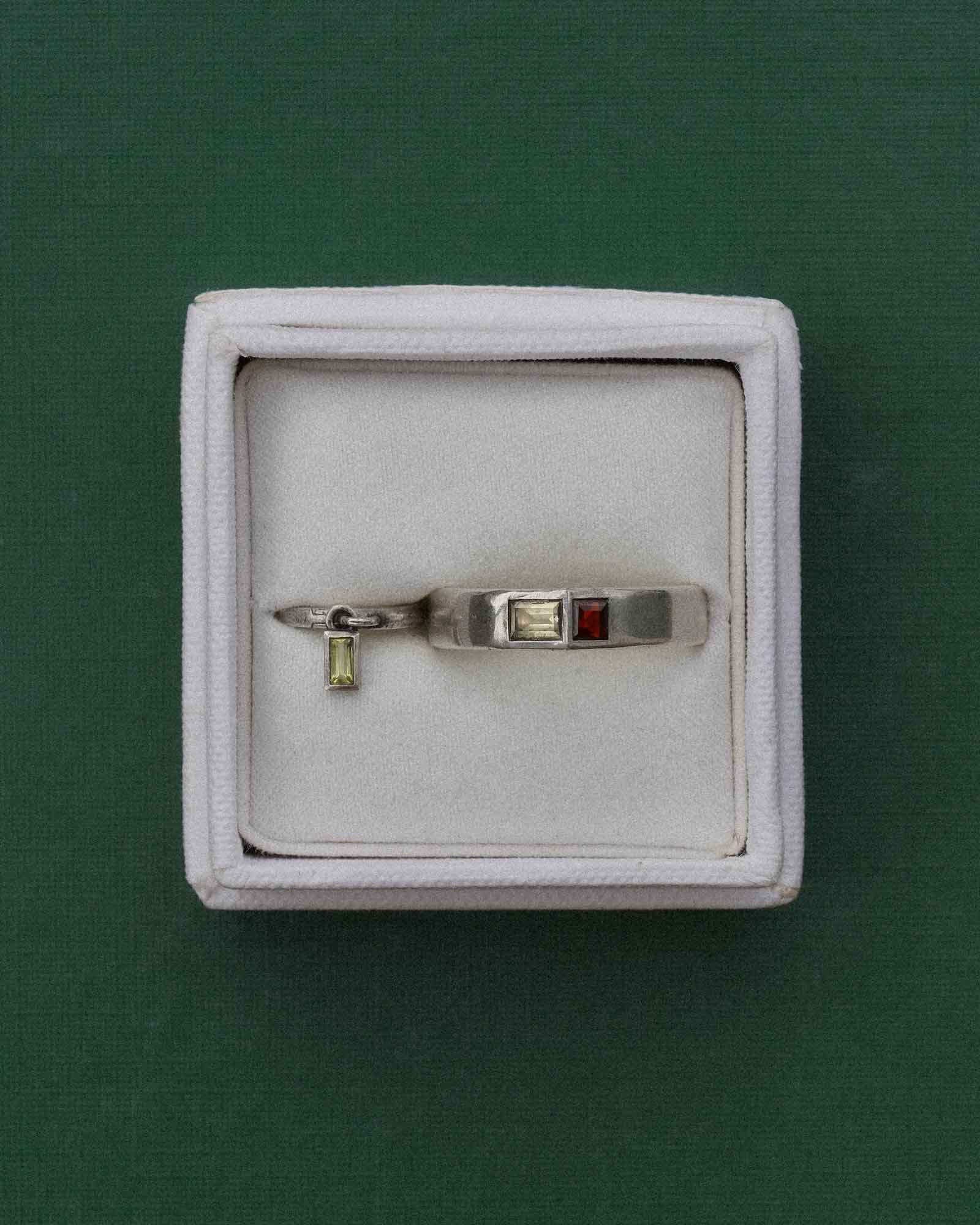 Silver ring and earring with gemstones in a white box on a green background