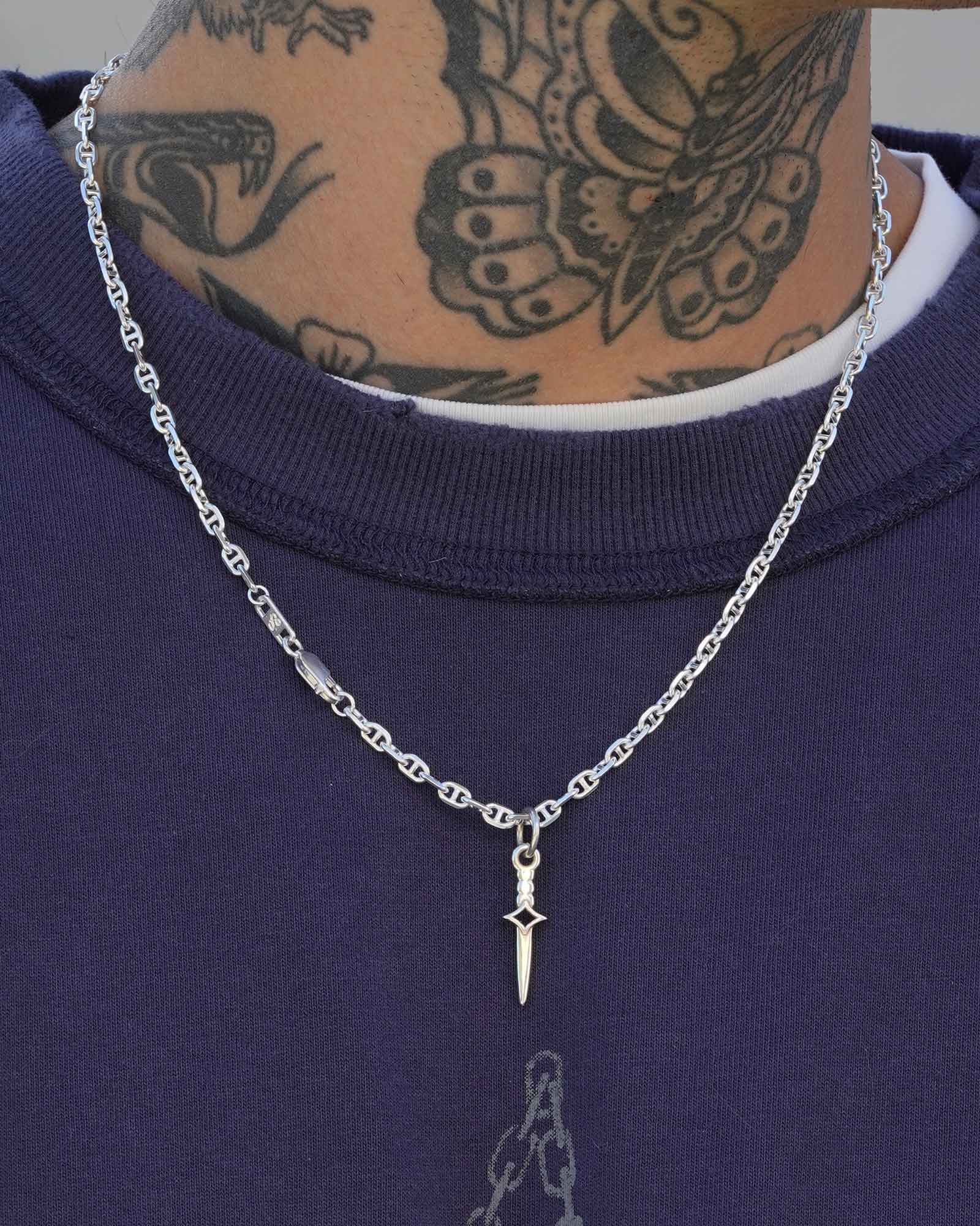 Silver chain necklace with a dagger blade pendant worn by a person with tattoos on their neck.