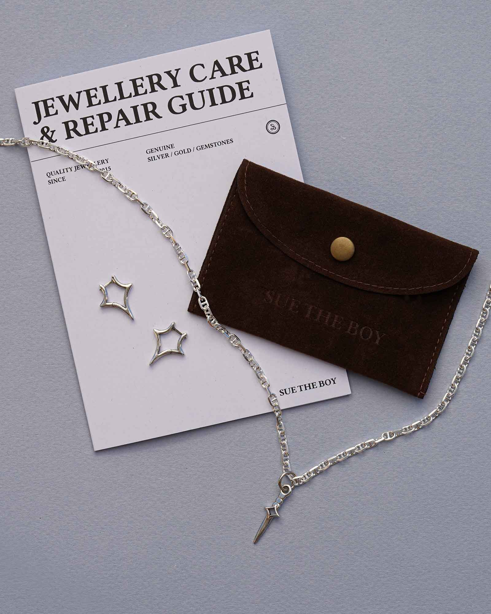 Jewellery set with necklace, pendant, earrings, and care guide on a gray background