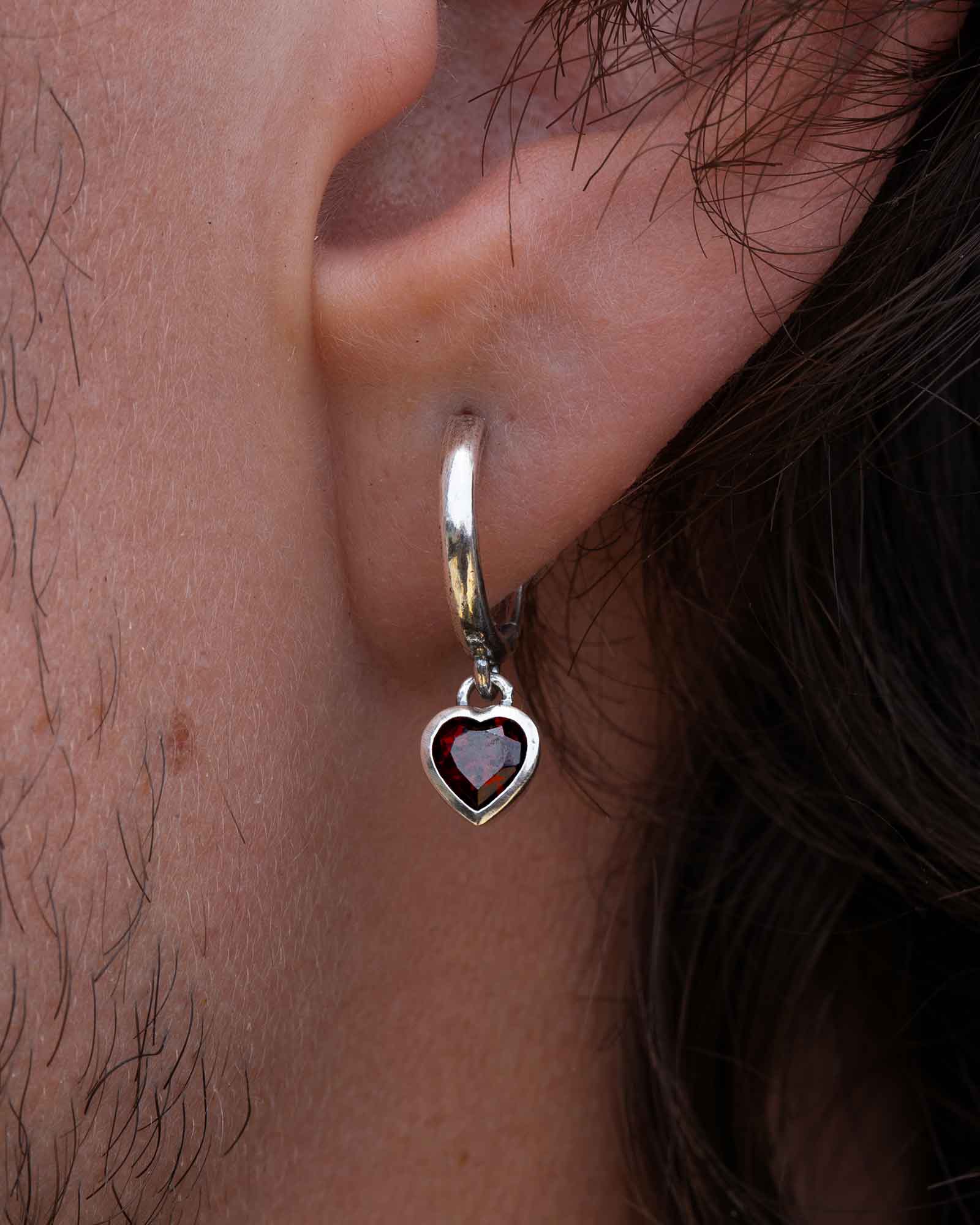 Close up of a silver hoop earring with a heart-shaped gemstone worn by a person.