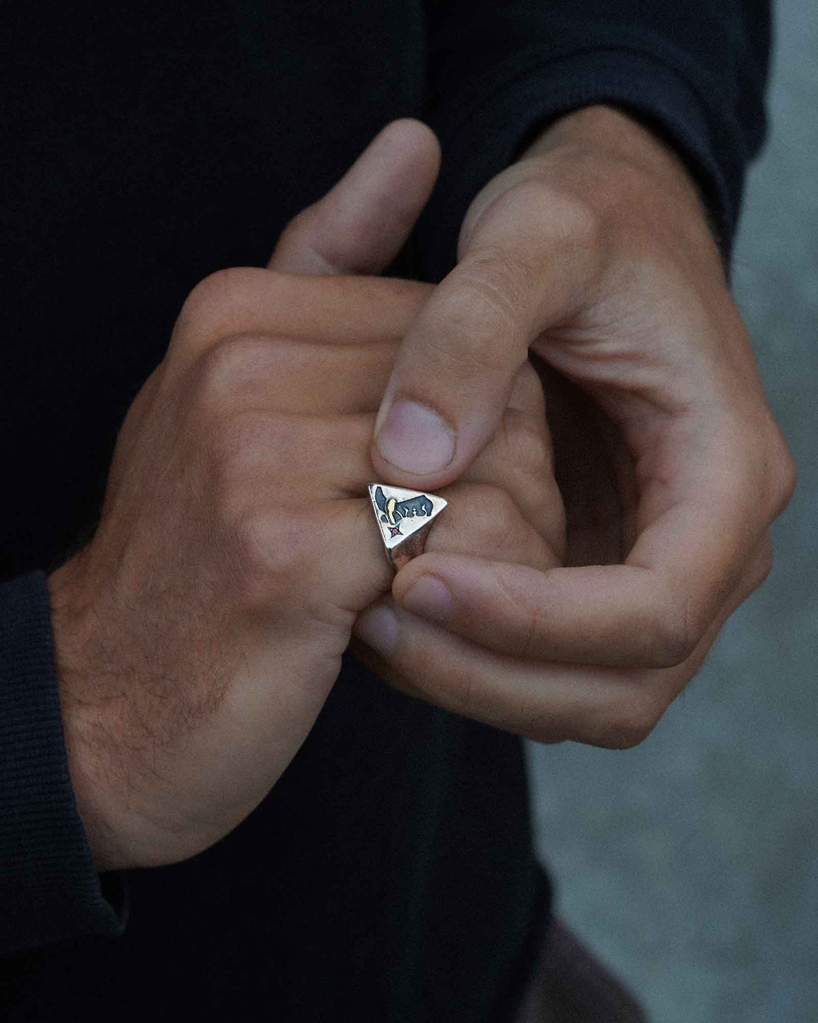 Close-up of a hand wearing a silver ring with a cowboy boot design on a blurred background