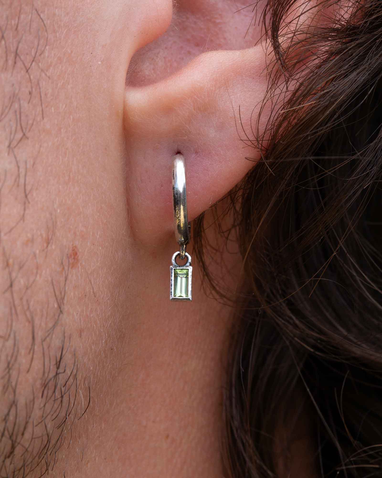 Close-up of an ear wearing a silver hoop earring with a small pendant.