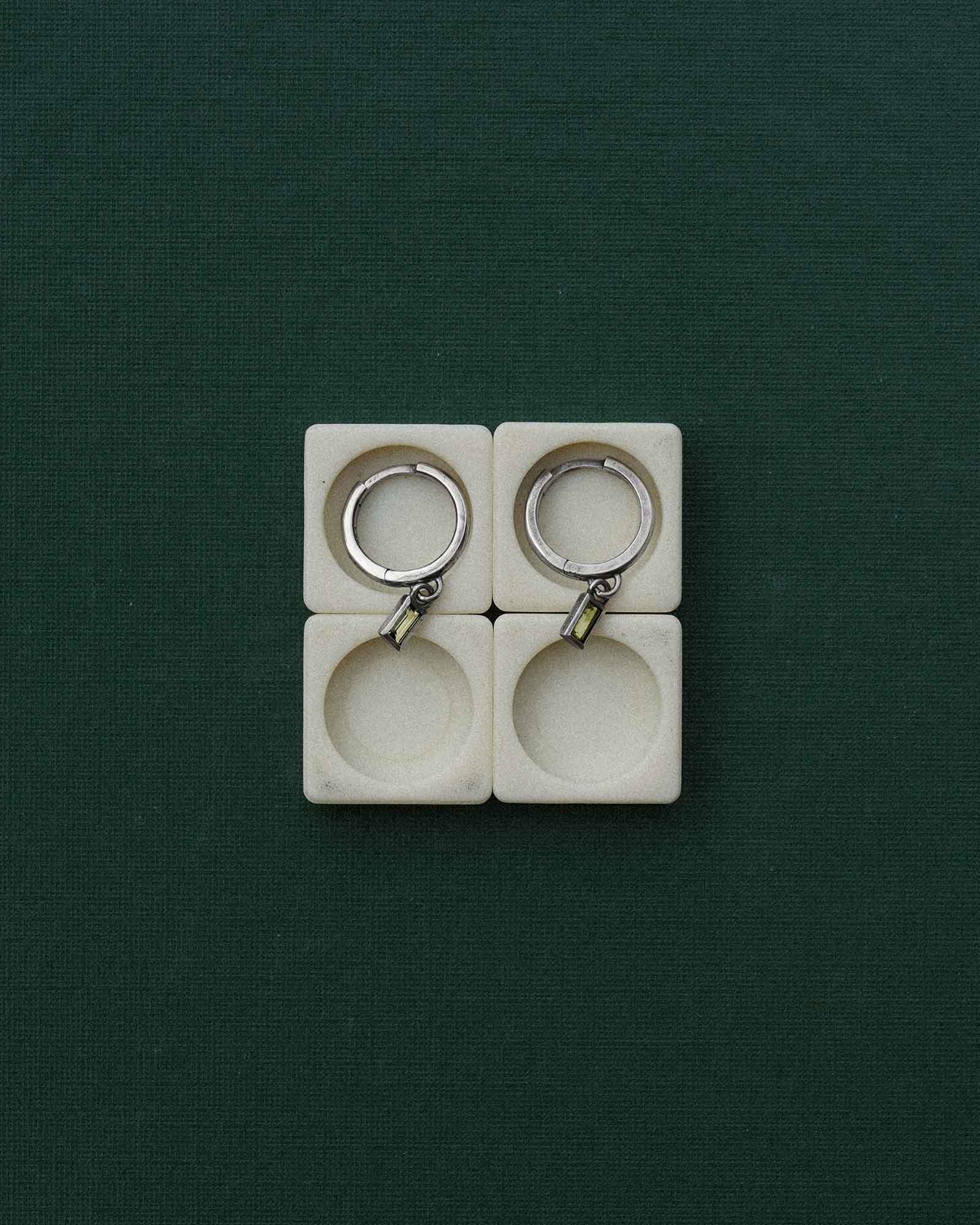 Two silver earrings in a white square mold on a green background