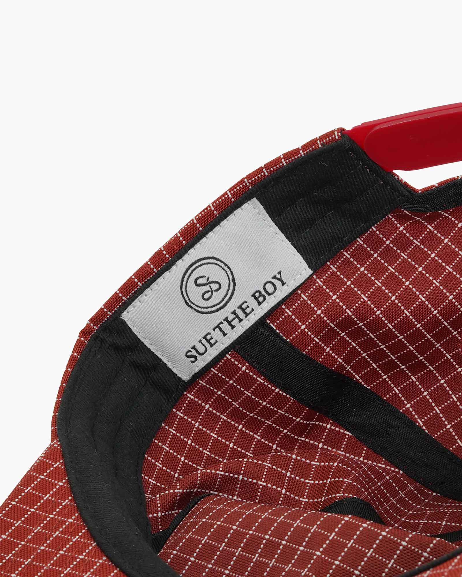 Inside of a red checkered cap featuring a black rim and a stitched on Sue The Boy label on a plain white background
