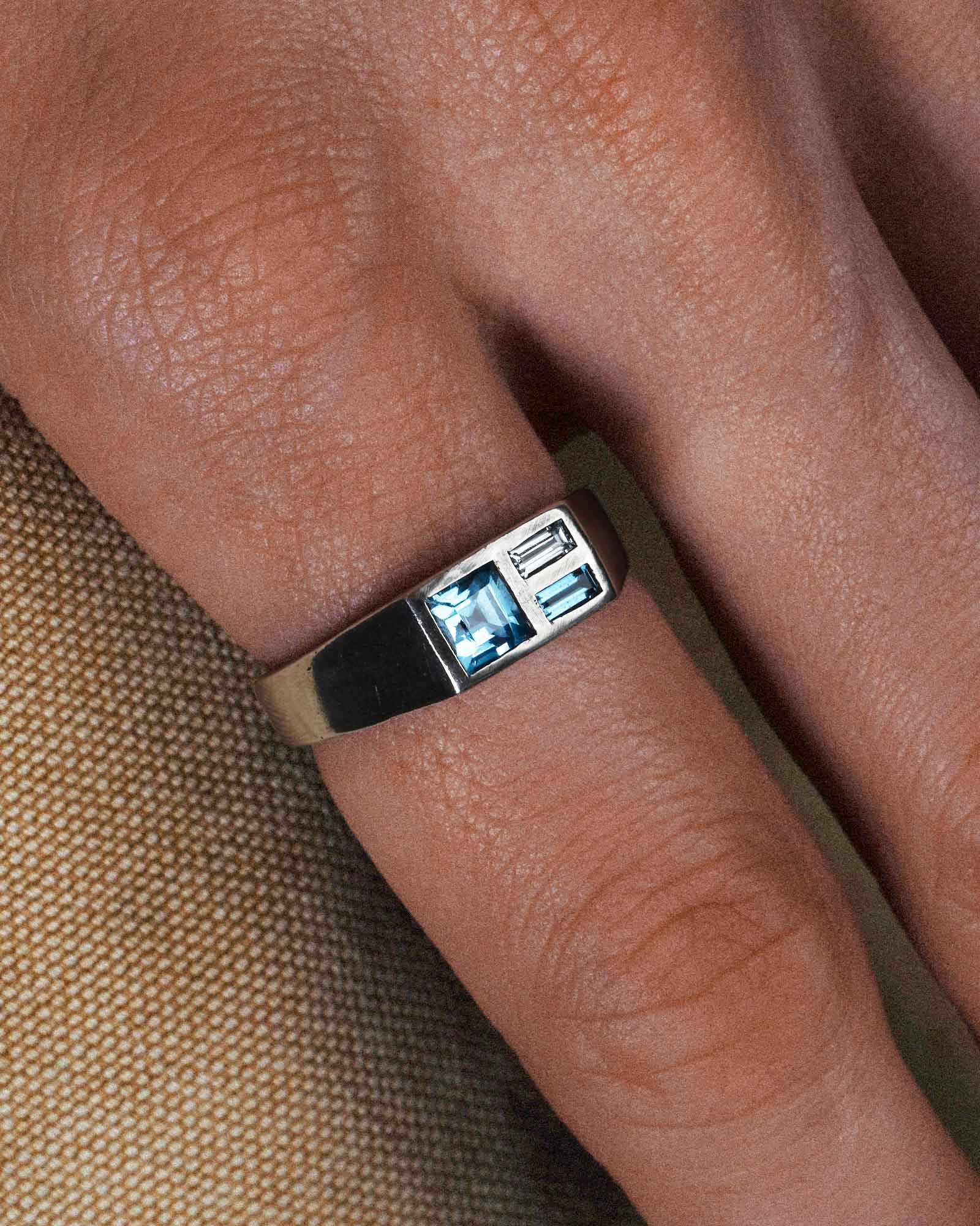 Silver ring with a blue gemstone on a finger against a brown fabric background