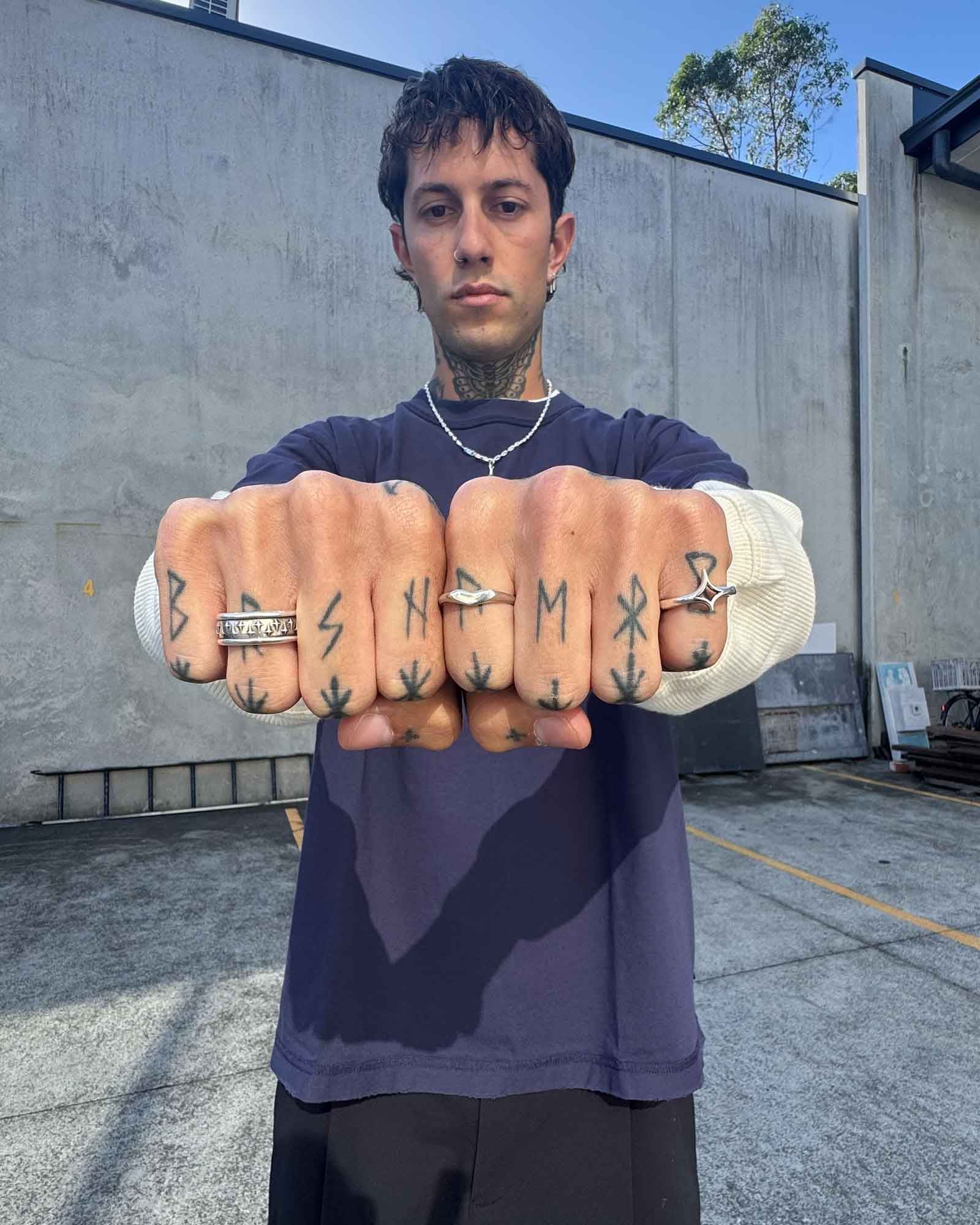 Person wearing multiple rings with tattoos on hands clenched in fists 