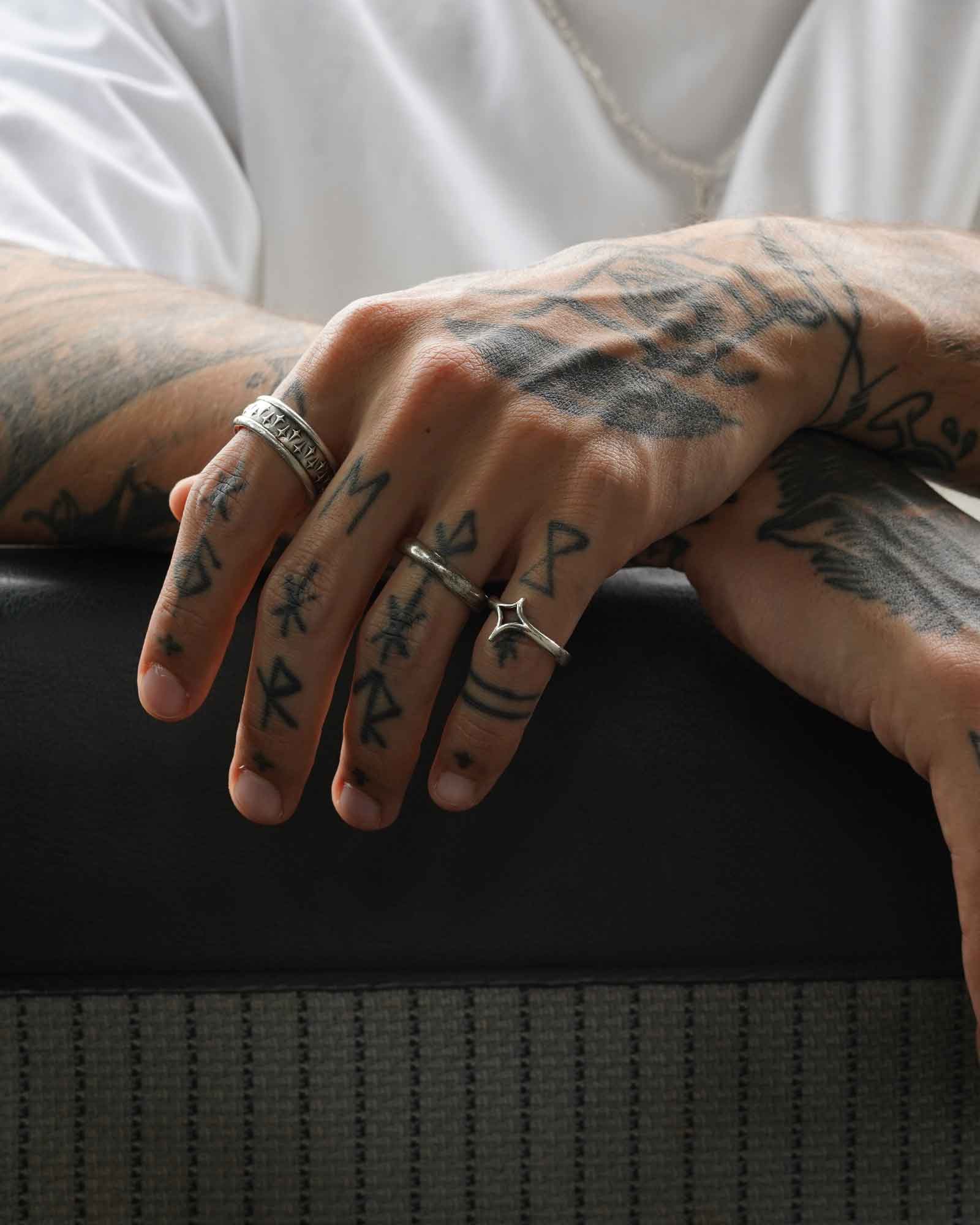 Close-up of a person's hands with tattoos and rings on a dark surface
