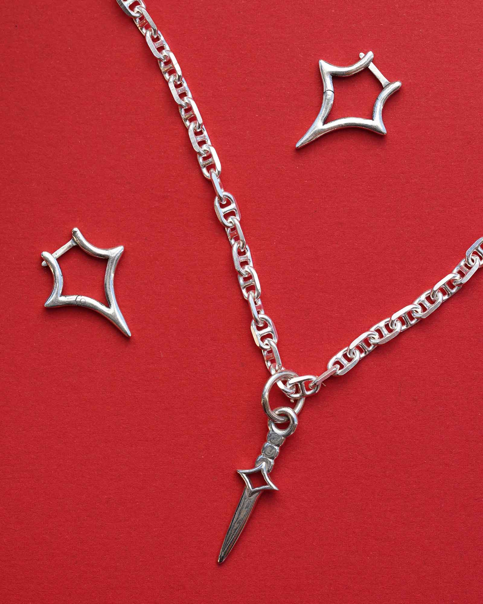 Silver necklace with dagger charm and two star shaped earrings on a red background