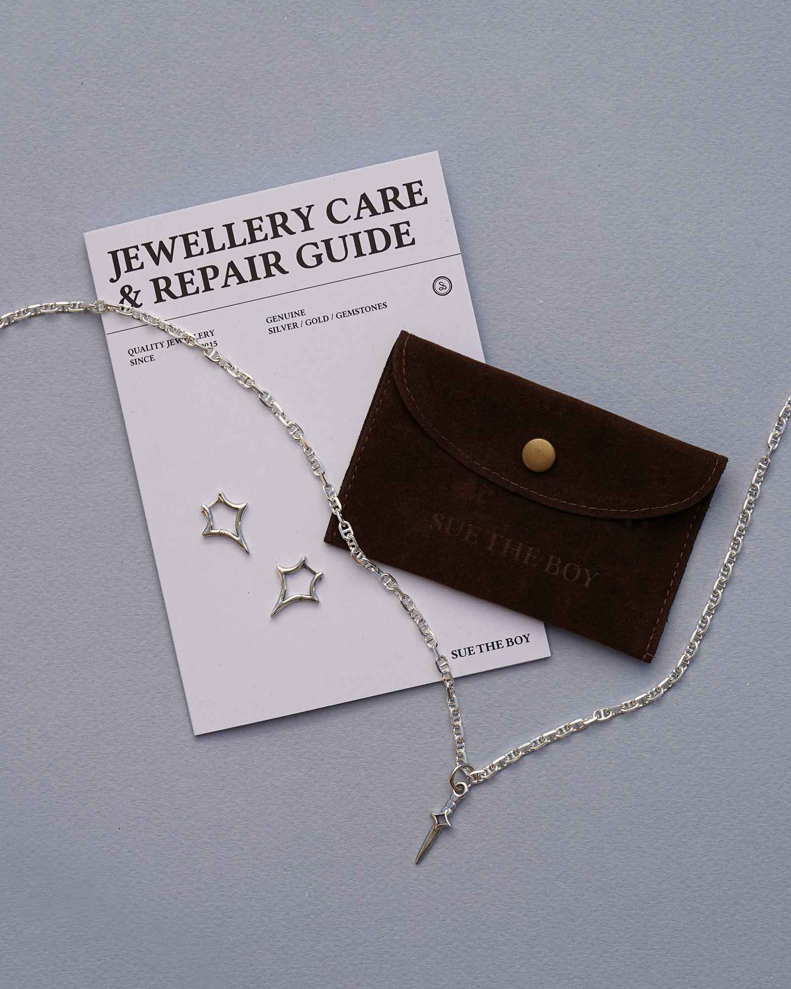 Jewelry set with necklace, earrings, and care guide on a gray background