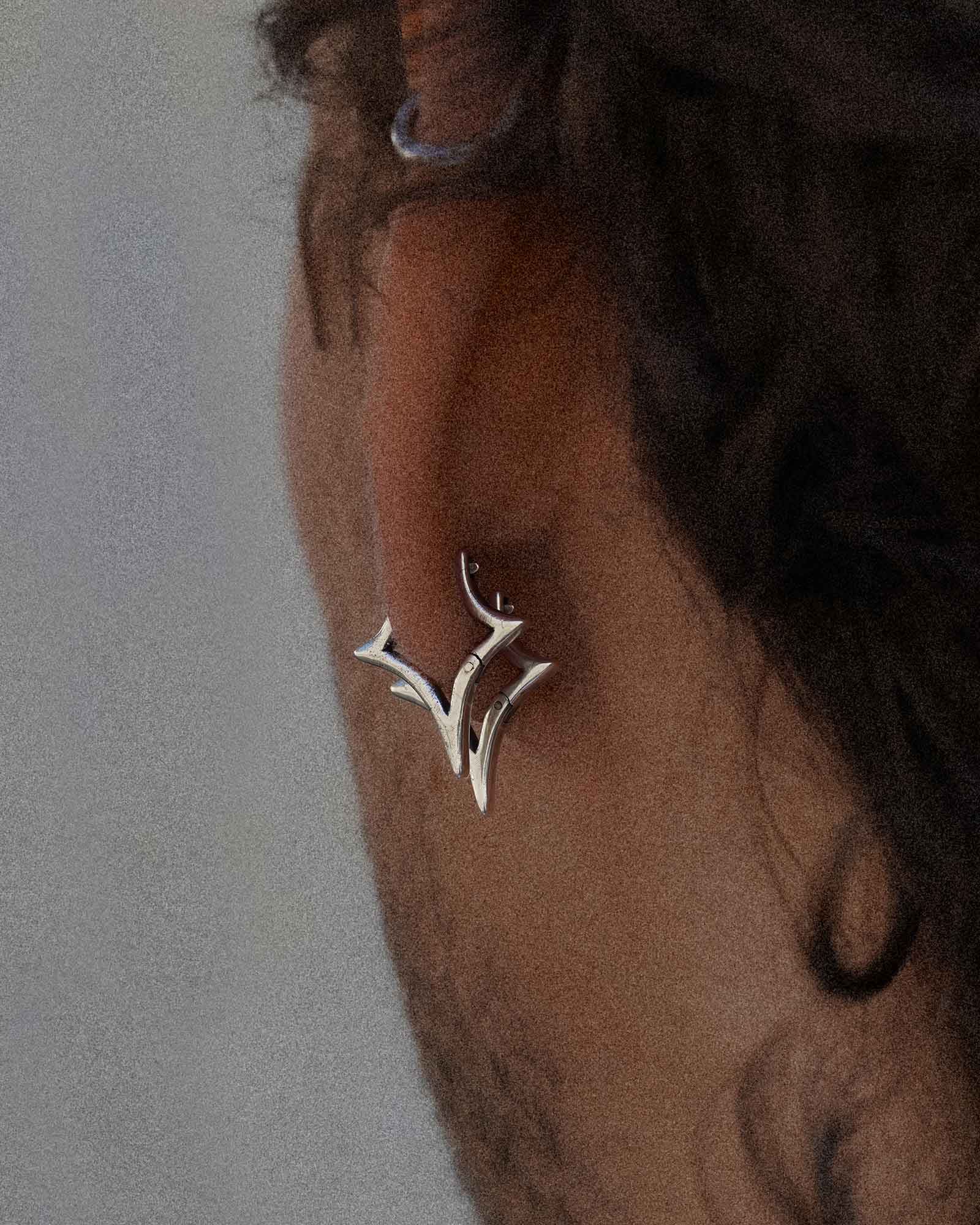Star shaped silver earrings worn by a person with a neutral background