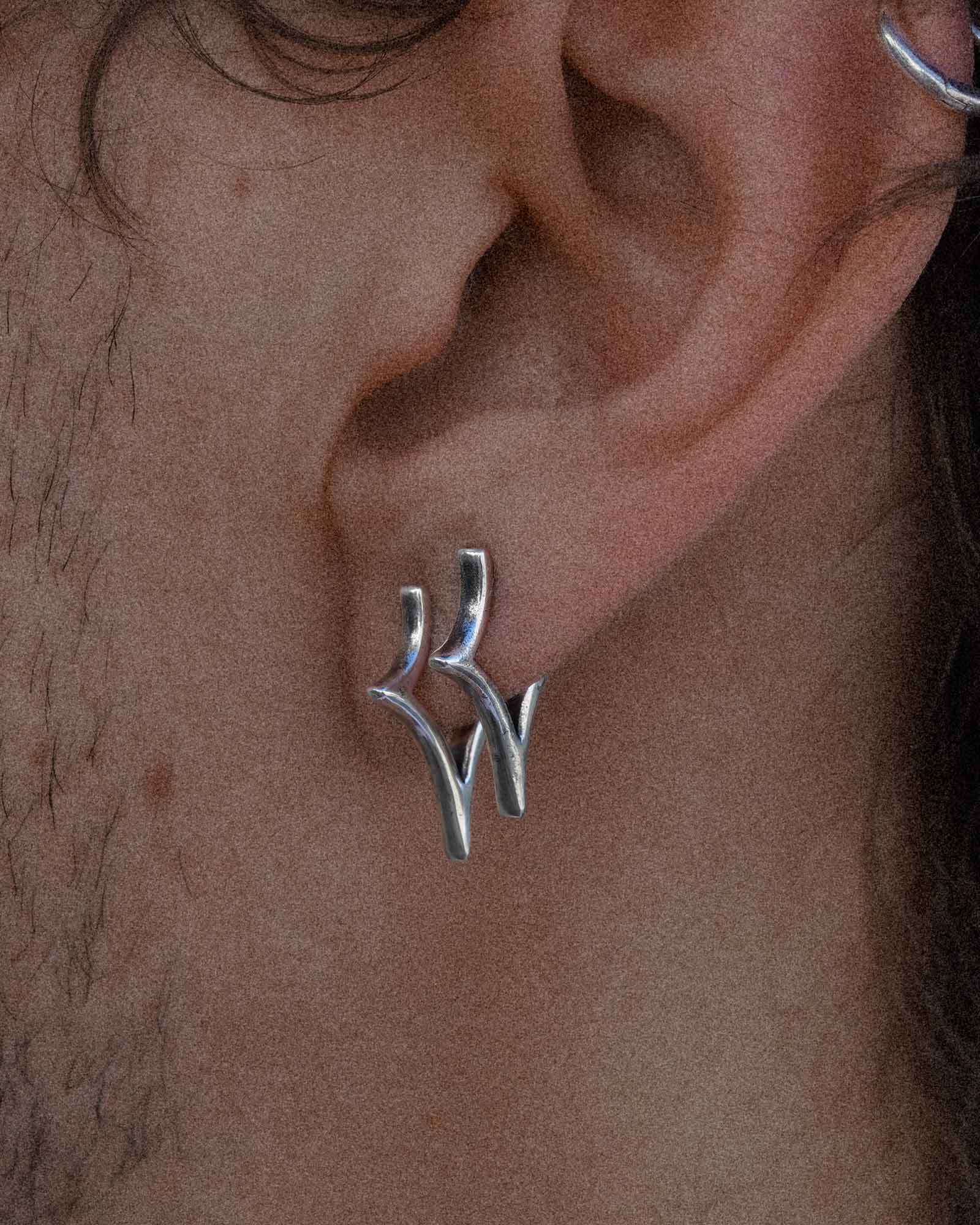Silver earring worn on an ear with a close-up view of the jewelry.