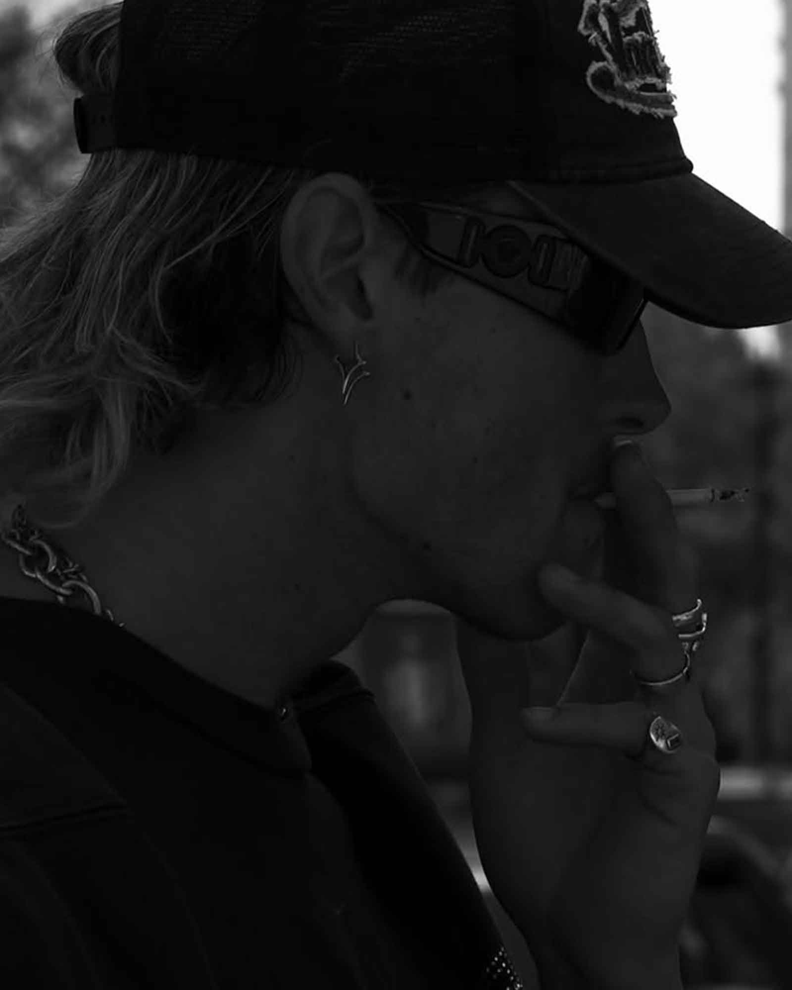 Black and white close-up of a person wearing a cap wearing silver earrings and rings.
