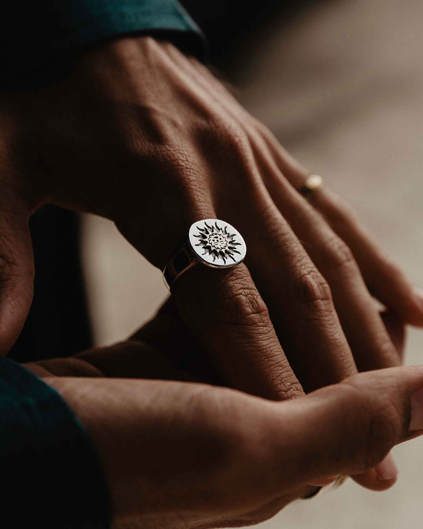 Close-up of a hand wearing a silver ring with a brass sun design on a blurred background