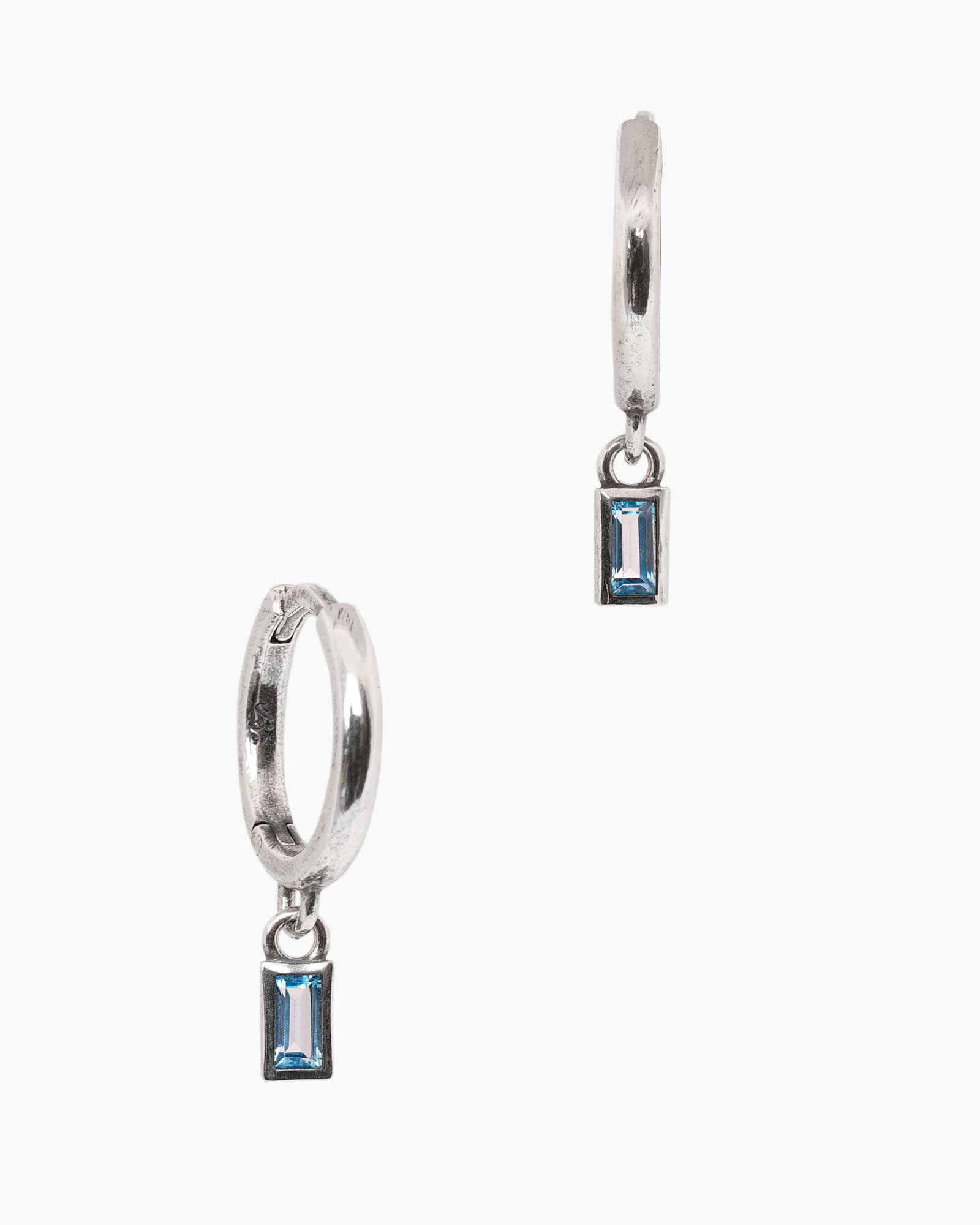 Pair of silver hoop earrings with blue gemstones on a white background