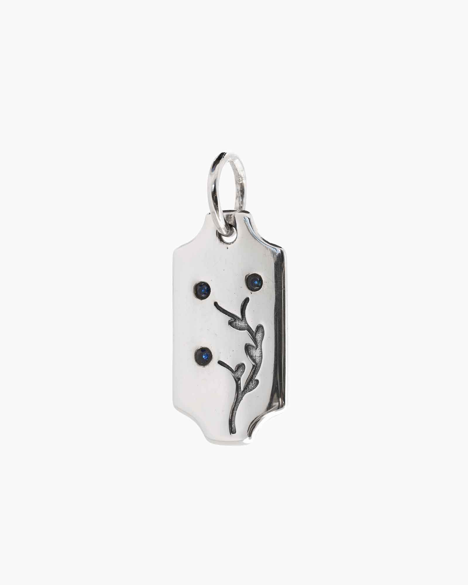 A silver rectangular pendant charm with a ring at the top, featuring an engraved violet motif and four small round stones, shown on a plain light gray background.