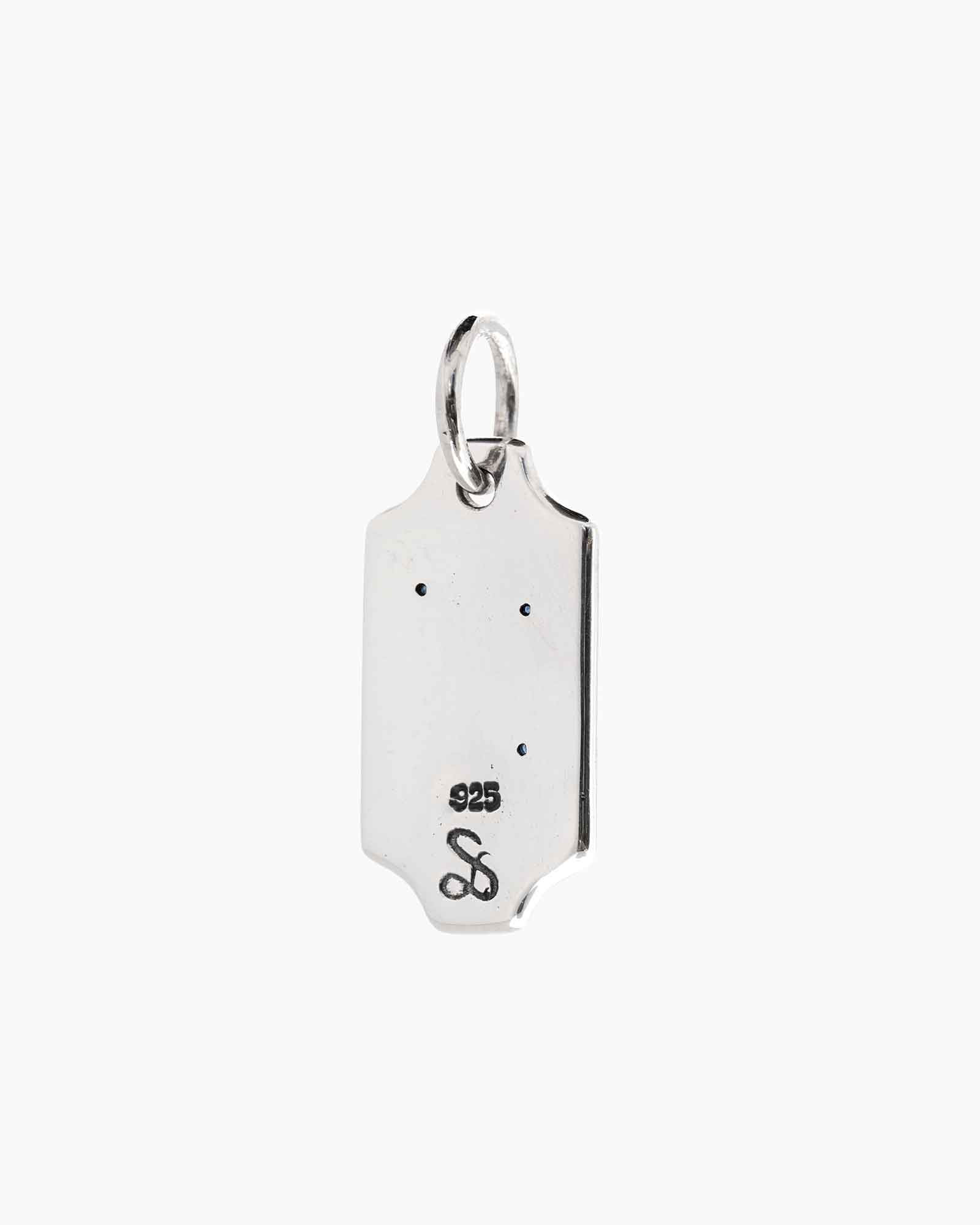 A silver rectangular pendant charm with a ring at the top, featuring an engraved sue the boy logo  and 925 stamp on a plain light grey background.