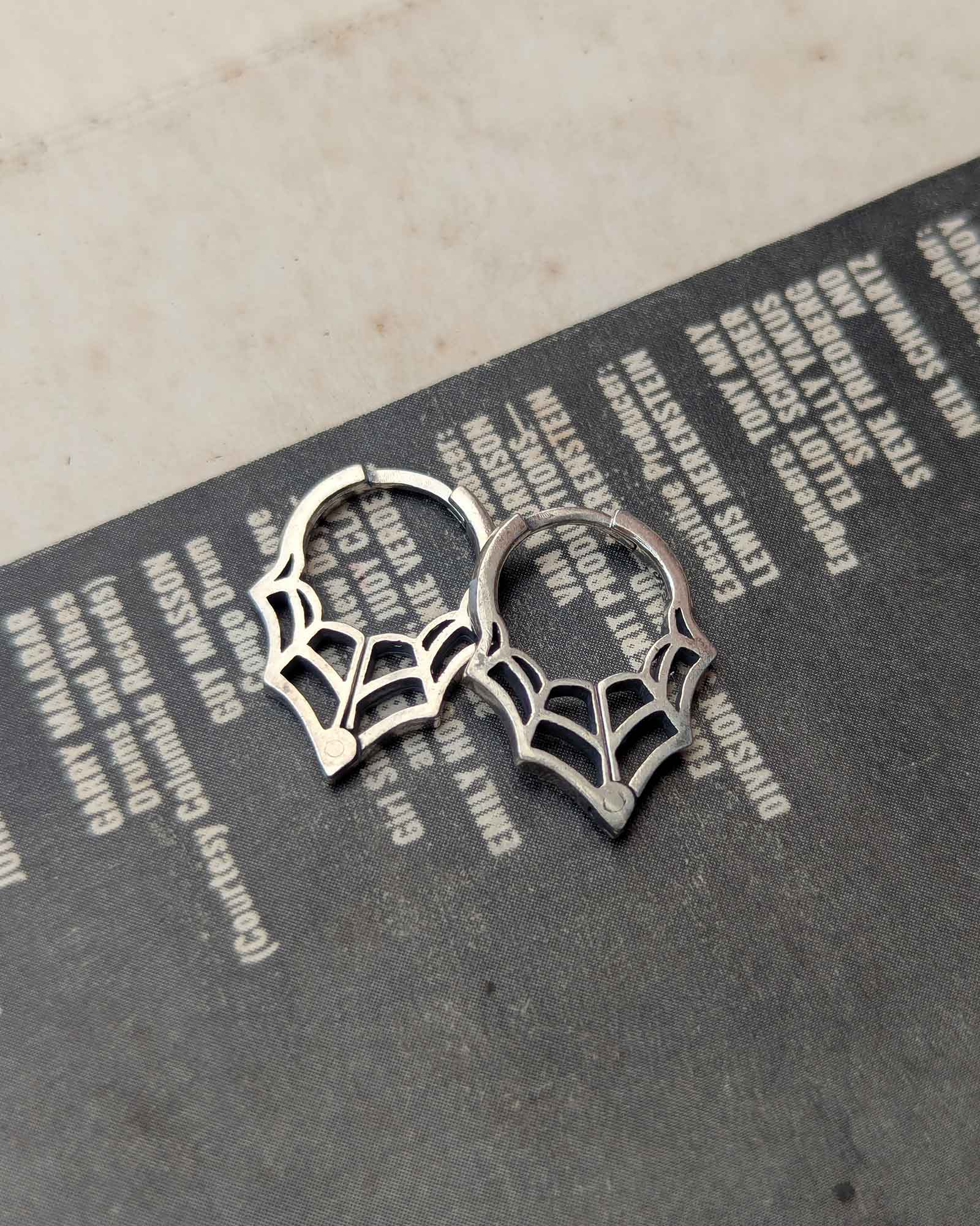 Pair of silver spider web earrings on a vinyl