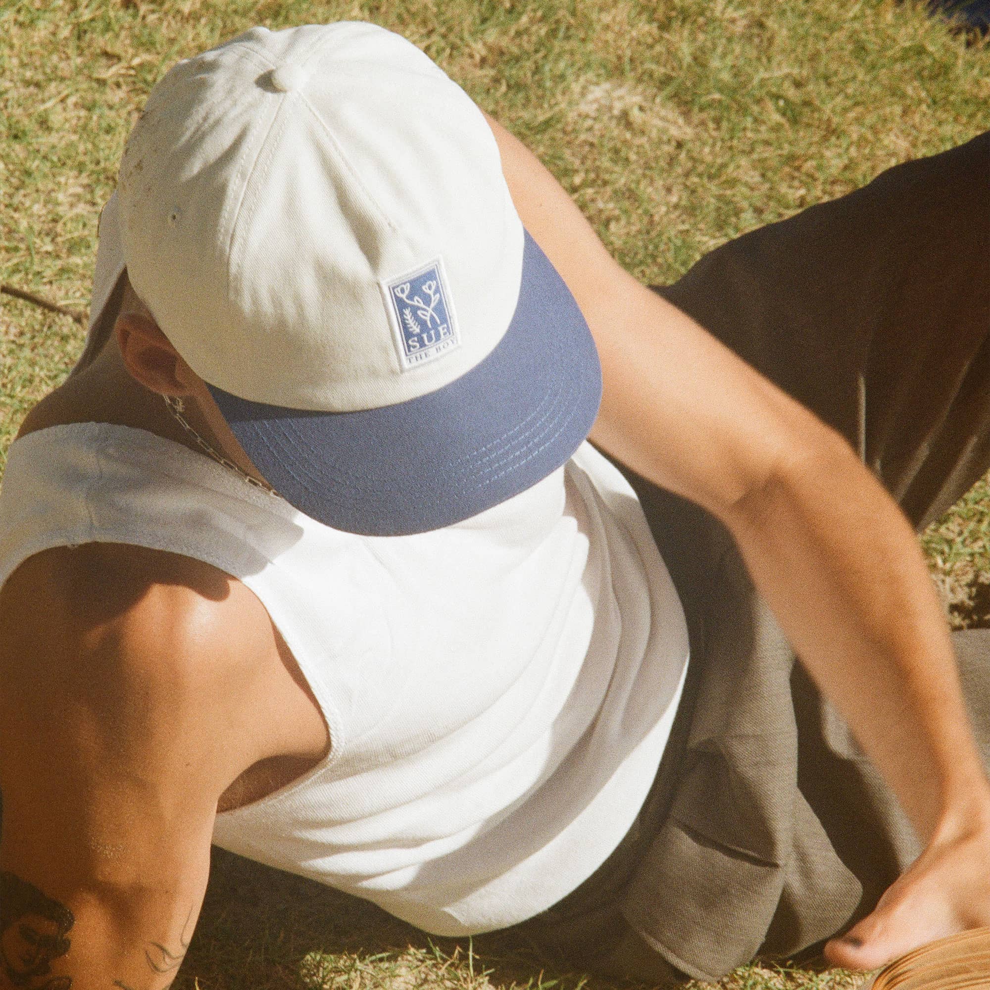 Man Wearing a White 5-Panel Cap With A Royal Blue Brim & Blue Woven Flower Patch